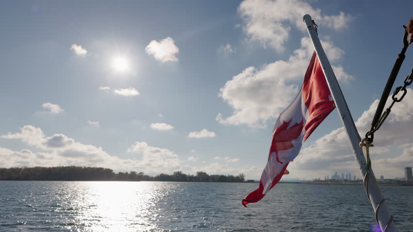 Canadian flag waving on boat with sun reflection on Lake Ontario water, bright travel scene with blue sky and clouds over calm horizon.