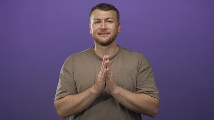 Man with hands pressed together in pleading gesture in studio against purple wall, young heavyset; hope humility.