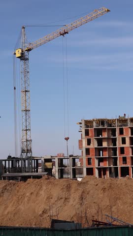 A yellow tower crane is operating at a residential complex construction site, lifting cargo against the backdrop of the new building and the blue sky