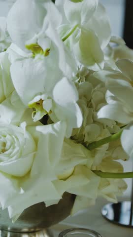 Vertical video. White roses close-up. Elegant arrangement of white flowers on a restaurant table, perfectly placed in a stunning silver vase.