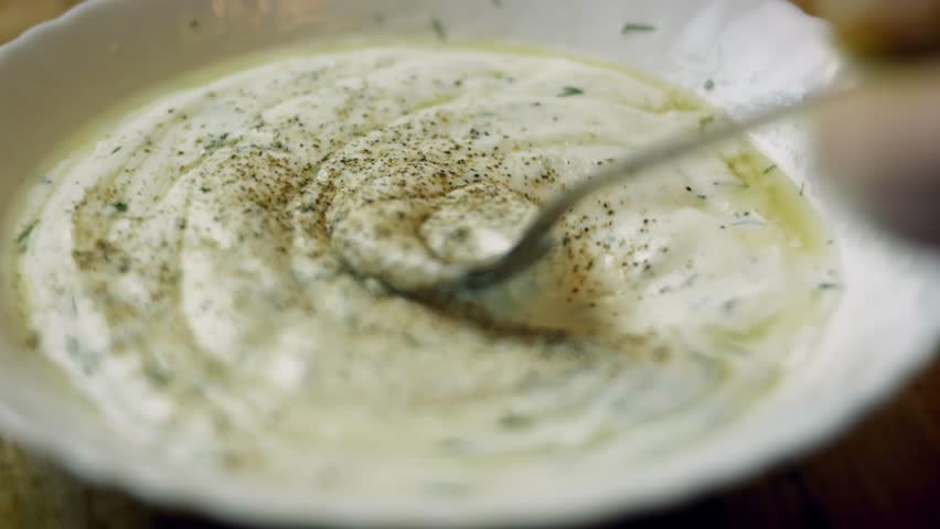 Close up of salt and black pepper being mixed with a yogurt dressing