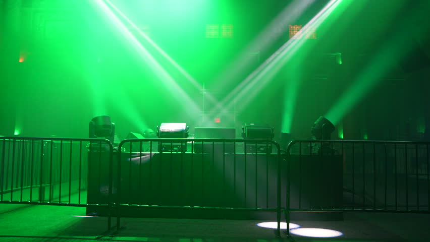 Dynamic white light beams cut through a dark, hazy space, illuminated by vibrant green ambient light. This abstract background captures the energetic atmosphere of a live concert or stage performance, ideal for event promotions and design projects.
