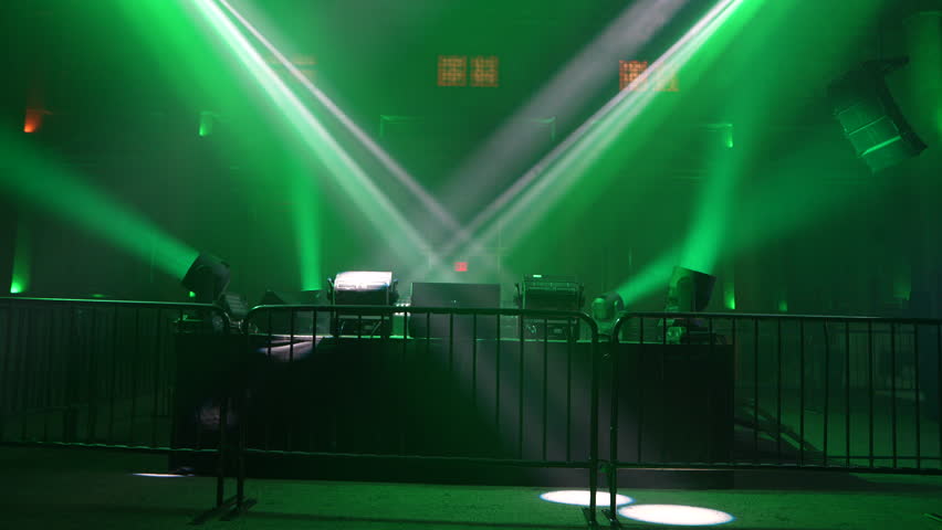 Dynamic white light beams cut through a dark, hazy space, illuminated by vibrant green ambient light. This abstract background captures the energetic atmosphere of a live concert or stage performance, ideal for event promotions and design projects.
