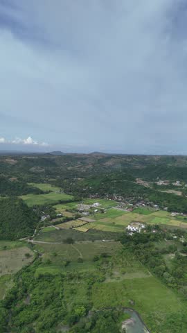Aerial View of Lush Green Rural Valley with Farmland, Village, and Distant Hills Under a Cloudy Sky