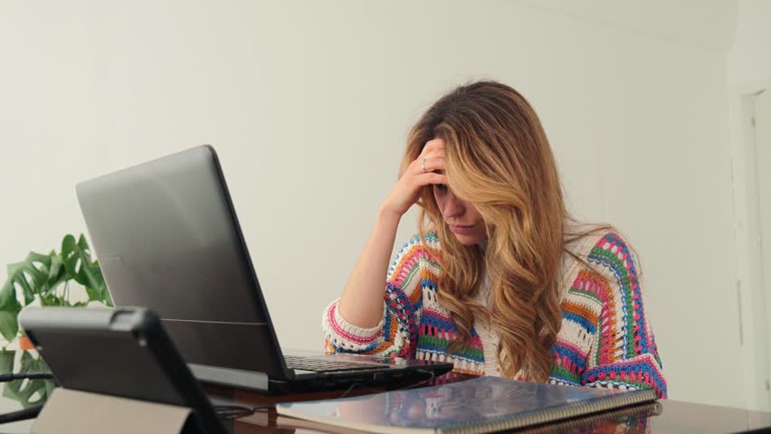 A stressed woman is focused on her laptop, feeling overwhelmed while trying to tackle her workload and manage her stress levels during a challenging workday or study session.