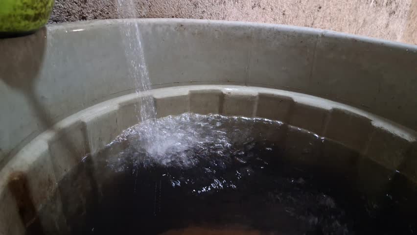Water pouring into tub close up view plastic bucket filling splash liquid storage resource management household sustainability concept highlighting water scarcity and essential basic needs for hygiene