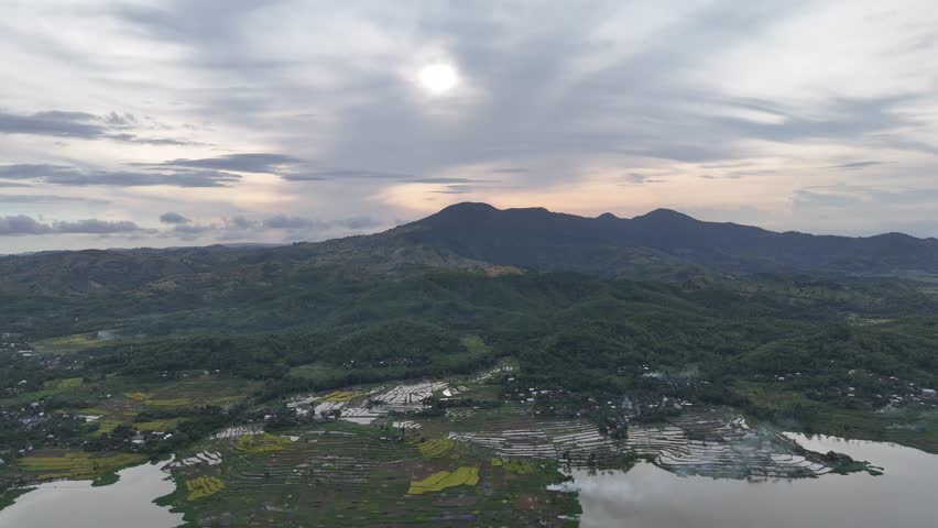 Aerial View of a Lush Mountainous Landscape with Terraced Rice Paddies and Serene Lake under a Cloudy Sky