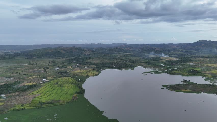 Aerial View of Lush Green Rice Terraces and Serene Lake Amidst Rolling Hills Under Overcast Sky