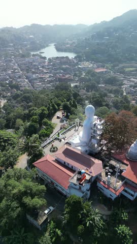 Aerial view of the giant white Bahirawakanda Buddha Statue on a hilltop overlooking Kandy, Sri Lanka. Cinematic drone shot of the famous religious monument and landmark.