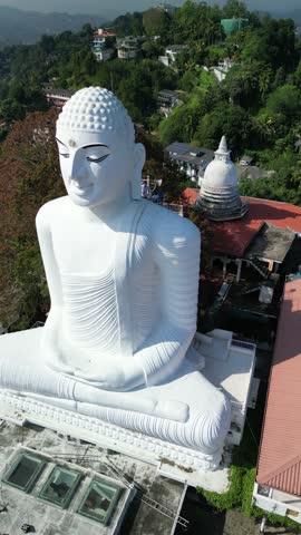 Aerial view of the giant white Bahirawakanda Buddha Statue on a hilltop overlooking Kandy, Sri Lanka. Cinematic drone shot of the famous religious monument and landmark.