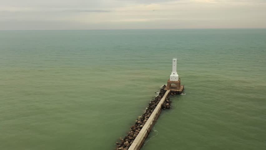 Drone aerial view of Port Washington Breakwater Light extending into Lake Michigan in Wisconsin, USA. Moody overcast sky, calm green water, and minimal coastal landscape create a serene atmospheric travel and landmark scene