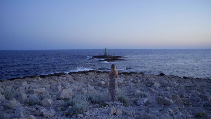Blonde woman in summer dress walking  outdoors in nature close the sea in Croatia. Beautiful evening at sunset.