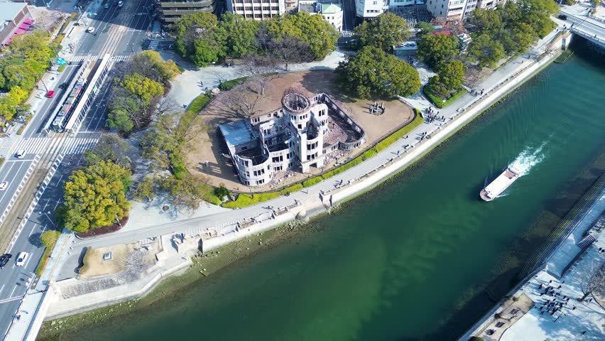 Drone aerial landscape of ferry boat passing by the historic Atomic Genbaku Dome structure hall building along the Motoyasu river near Peace Park Memorial in Hiroshima city Japan tourism and travel