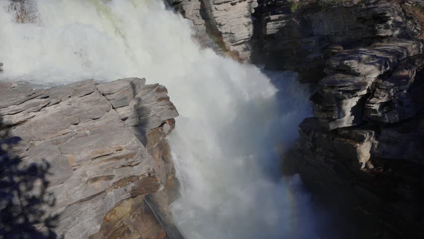 Powerful Athabasca falls cascading over rocks with mountains and forest in Jasper National Park, Canada