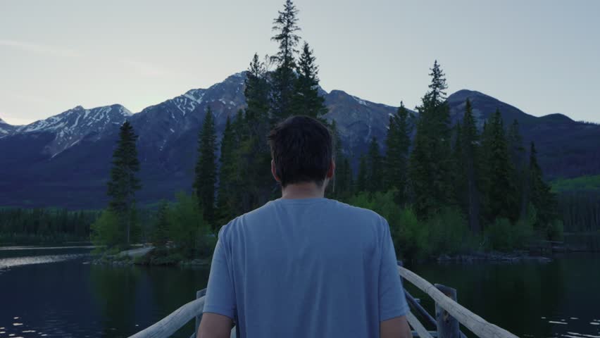 Man walking across a wooden bridge towards a forested island on Pyramid Lake in Jasper national park, Canada