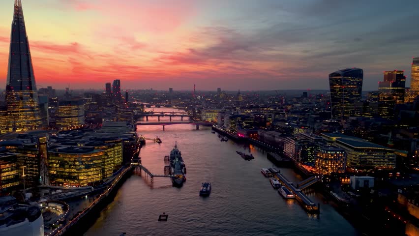 Establishing aerial view towards the Tower Bridge in London, England, with city skyline and river Thames during dusk with a colorful sky