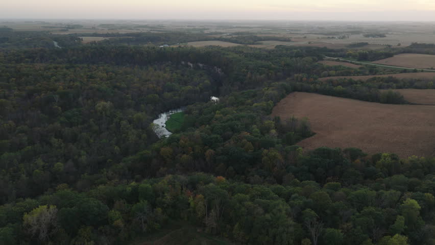 Aerial landscape of Root River winding through forest and farmland in Minnesota, panoramic descend drone