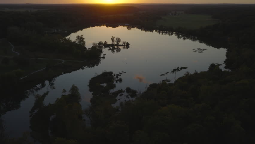 Aerial pullback tilt-up to forest lake at dusk sunset in Siloam Springs Arkansas as sun dips below horizon