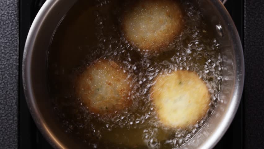 Shrimp cakes deep frying in hot oil, close up. Active bubbling and rapid frying motion with crispy texture forming on surface.