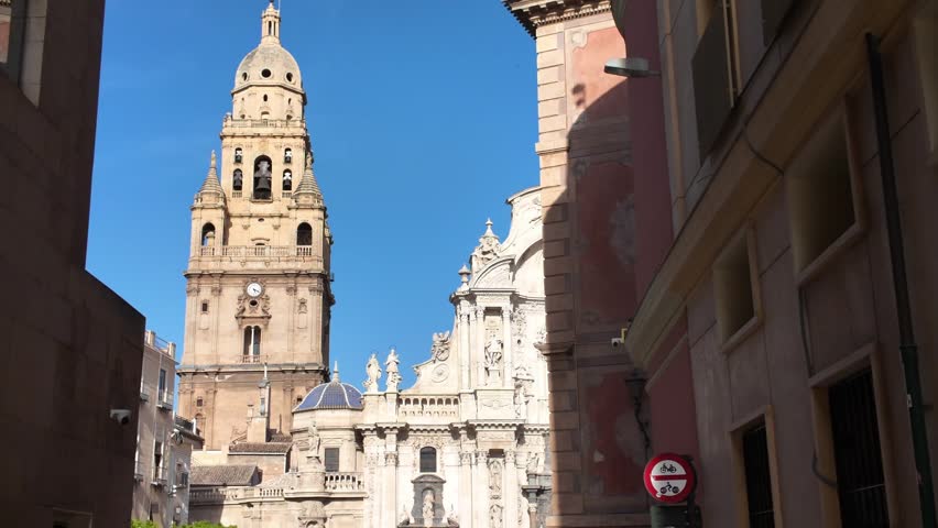 Historic Murcia Cathedral bell tower rising above traditional Spanish baroque architecture in sunny city center with blue sky and ancient stone facade