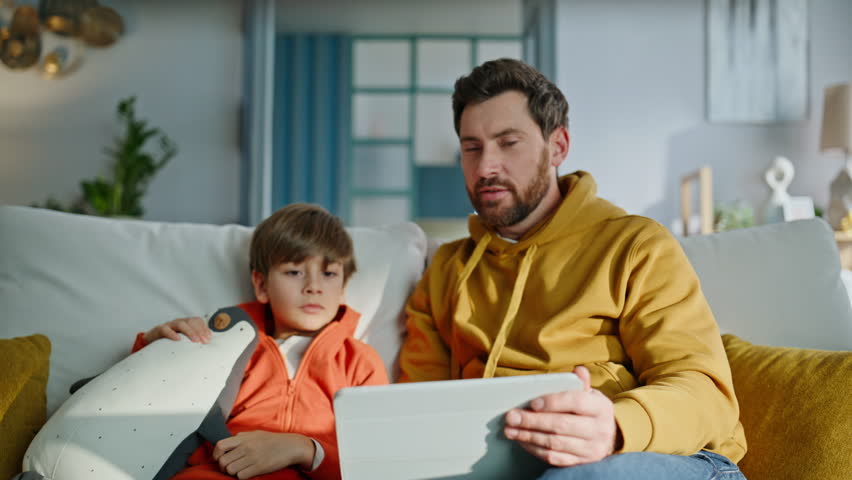 Father boy videocalling tablet sitting home sofa together closeup. Smiling bearded dad happy little boy talking at virtual meeting looking web camera pad computer. Family enjoy video call conversation