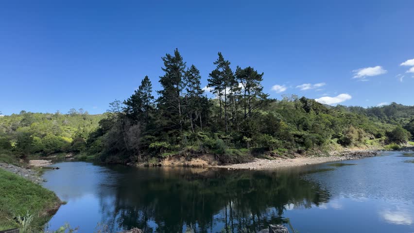 Clear blue river surrounded by lush green forest and trees, reflecting the landscape under a bright sky, creating a peaceful natural scene.