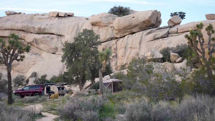 Teardrop camper trailer is parked at Joshua Tree National Park in California. A family sets up their camping area in the desert.