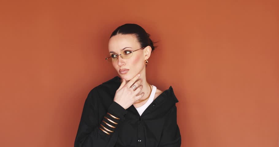 Excited young woman in yellow glasses having a great idea or eureka moment pointing finger up with happy facial expression and bright smile standing against terracotta background wall