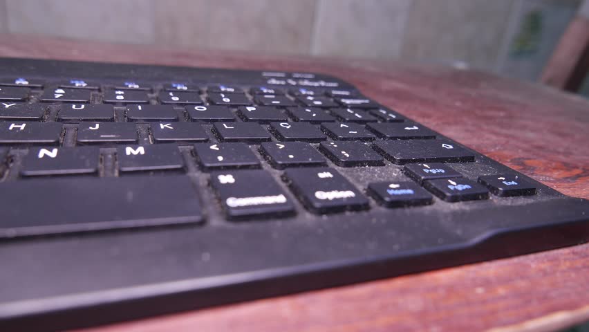 POV: Typing on a dusty keyboard. A Bluetooth keyboard. A laptop keyboard. Person typing with one hand. A QWERTY keyboard. Computer keys. Close-up shot. Office. Writing. 