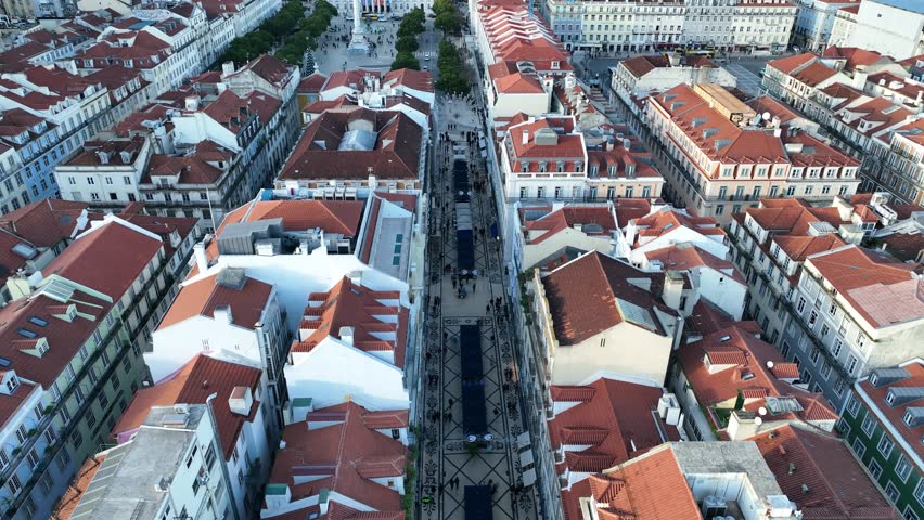Cinematic push-in shot flying over traditional terracotta rooftops to unveil Rossio Square in Lisbon, Portugal, during soft morning light, 4K aerial footage.