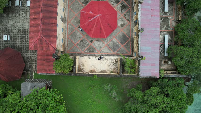 A top-down pull-out reveals the weathered ruins of Prison Island in Zanzibar, Tanzania, nestled within lush greenery beside turquoise coastal waters.