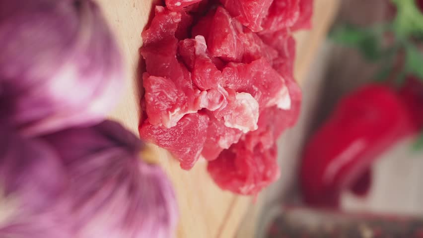 Macro view of fresh raw beef meat cubes on wooden cutting board with purple garlic and red chili pepper.