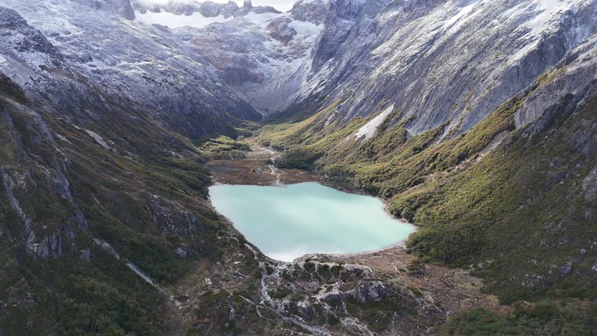 Stunning Aerial View of a Turquoise Glacial Lake Nestled Between Rugged Snow-Capped Mountain Peaks
