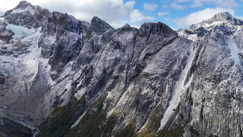 Aerial View of Majestic Snow-Capped Grey Mountains Under a Bright Blue Sky with White Clouds