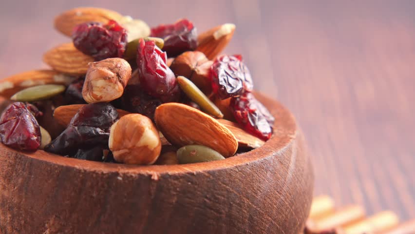 Healthy trail mix close up slow motion footage of nuts and dried fruits in wooden bowl.