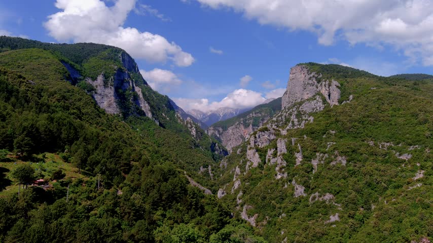 Aerial footage of Mount Olympus in northern Greece, showing steep rocky cliffs, deep forested valleys and dramatic mountain scenery under shifting clouds.
