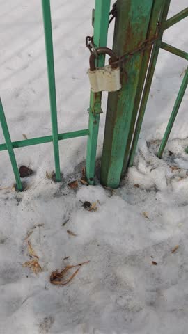 Green metal gate with a white padlock secured in snow-covered ground, showing gradual unlocking process in a winter outdoor setting