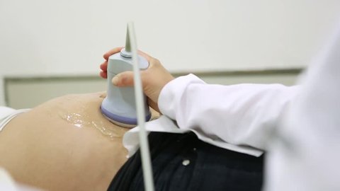 Close up detail of ultrasound probe moving over pregnant belly of woman