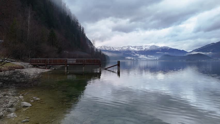 Aerial view of a tranquil mountain lake with a wooden pier and snowy peaks in the distance