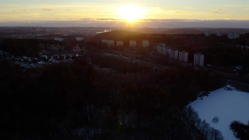Drone sunset view over Kortedala and Bergsjön in Gothenburg, Sweden, with forest, apartment buildings and winter light. Scenic urban panorama with warm evening glow and Nordic atmosphere.