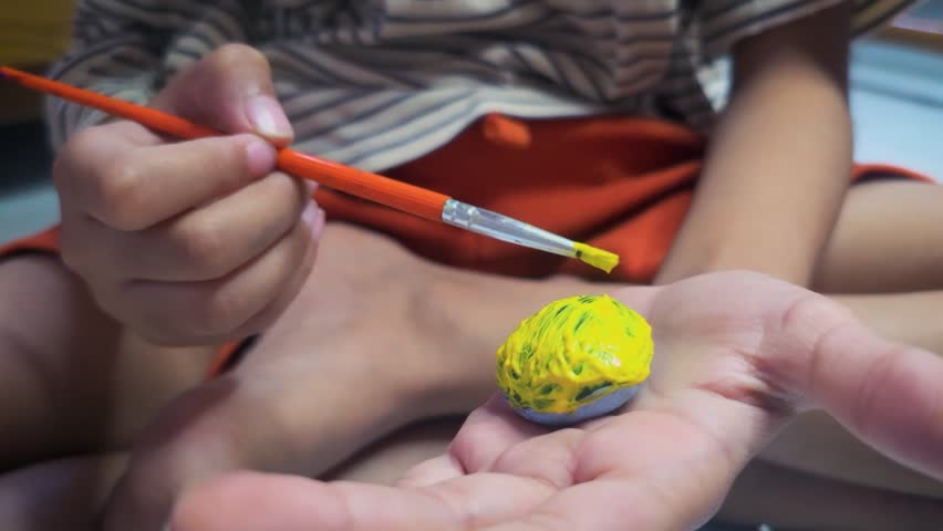 Close up shot of a kit painted a stone with yellow color with paint brush. painting activity