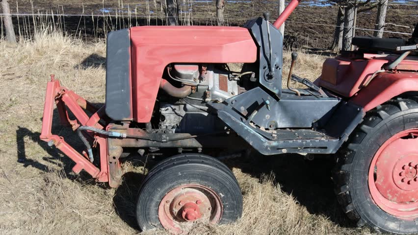 A vintage red tractor parked in a green field with a rustic backdrop.