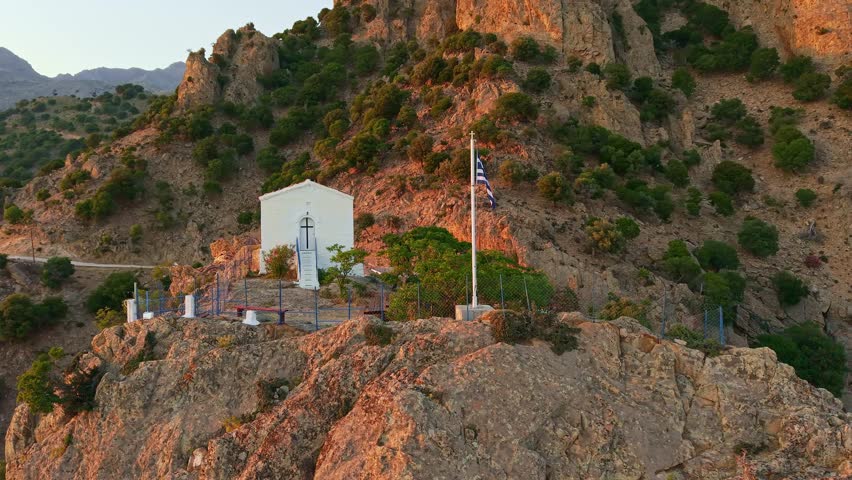Aerial view of the historic white chapel of Panagia Krimniotissa at sunset, perched on a high cliff overlooking the Aegean Sea and Pachia Ammos beach, Samothrace island, Greece