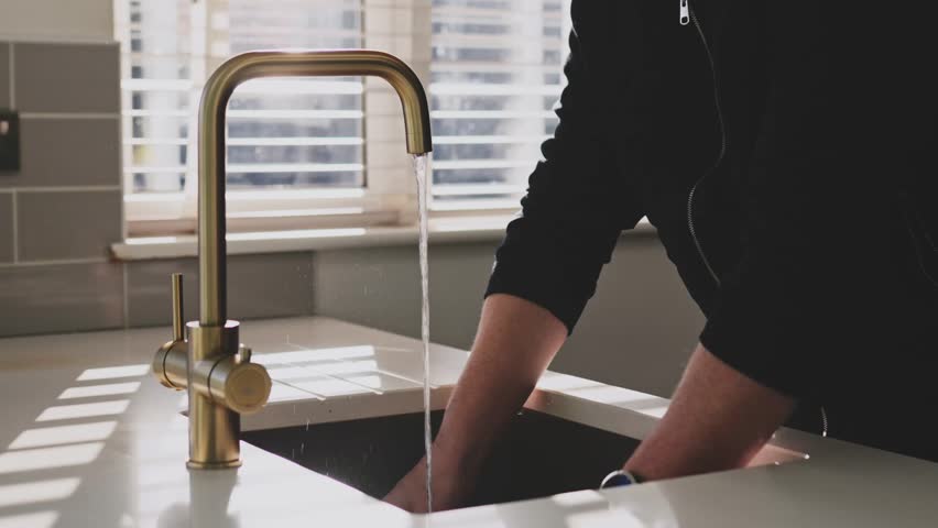 Man washing dishes at the kitchen sink faucet tap