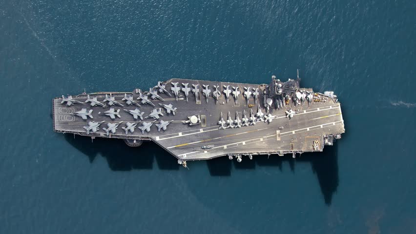 An aircraft carrier is positioned in the sea, displaying military power with fighter jets lined up on its deck. This naval vessel represents key maritime defense and operational readiness.