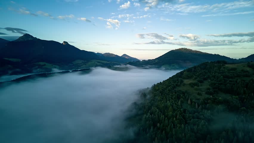 Aerial time lapse of thick morning mist flowing through mountain valley