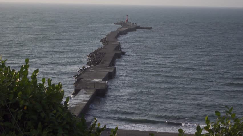 Cinematic shot of a long jetty heading out into the sea protecting the entrance to Kaohsiung Port.