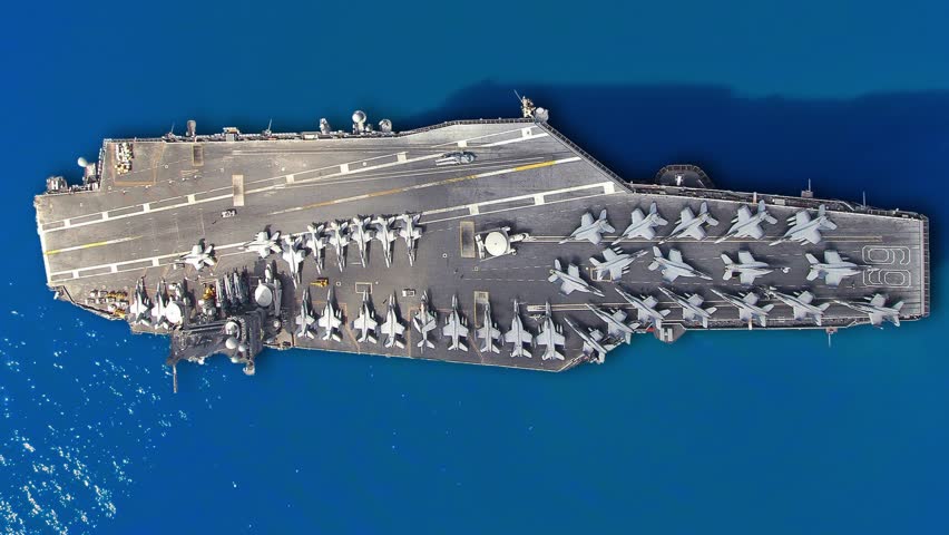An aircraft carrier is anchored with multiple military aircraft positioned on its deck.