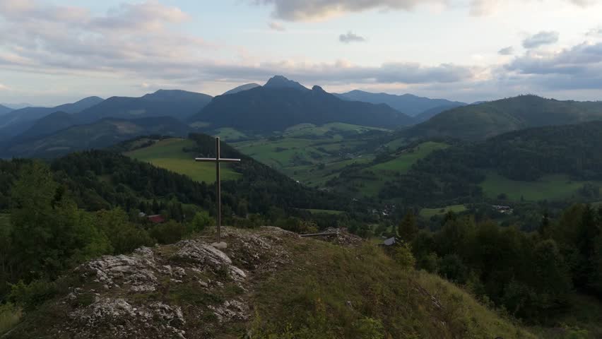 Aerial flyover of iron cross on rocky peak revealing mountain valley
