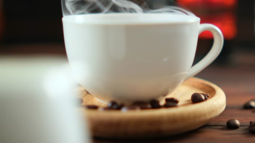 Fresh hot coffee in white cup with steam, coffee beans on wooden plate, warm cozy dark background, slow motion